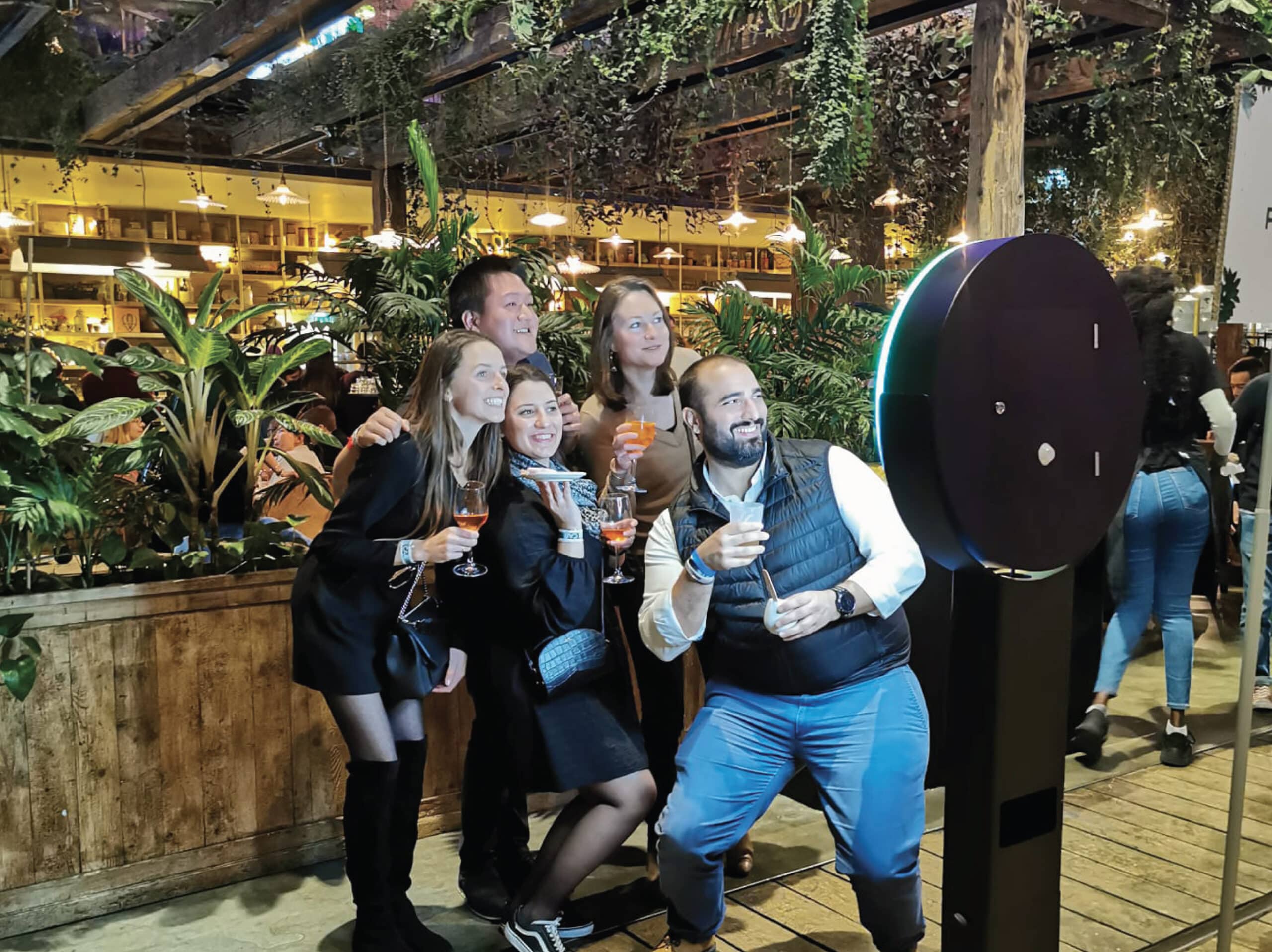 Groupe d'amis posant devant la borne photo Ring de Shootnbox dans un bar à la déco végétale