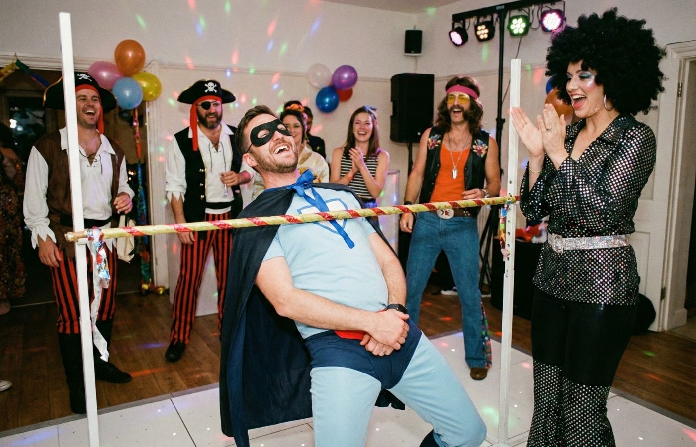 Amis déguisés en super-héros et disco jouant au limbo lors d'une fête d'anniversaire adulte rigolote.