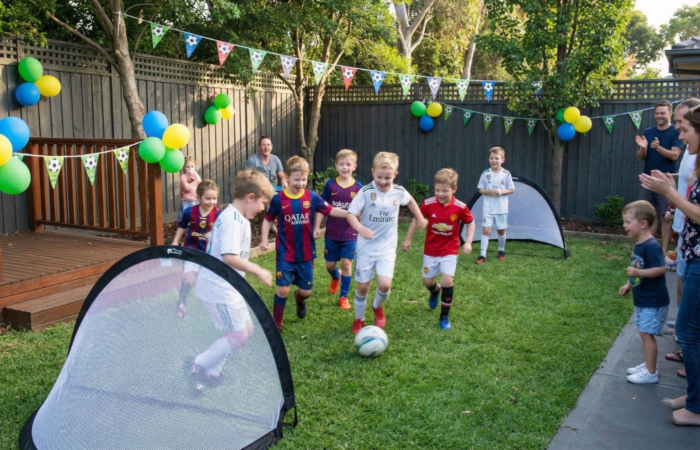 Groupe d'enfants joyeux en maillots de foot jouant un mini-tournoi dans un jardin décoré pour un anniversaire