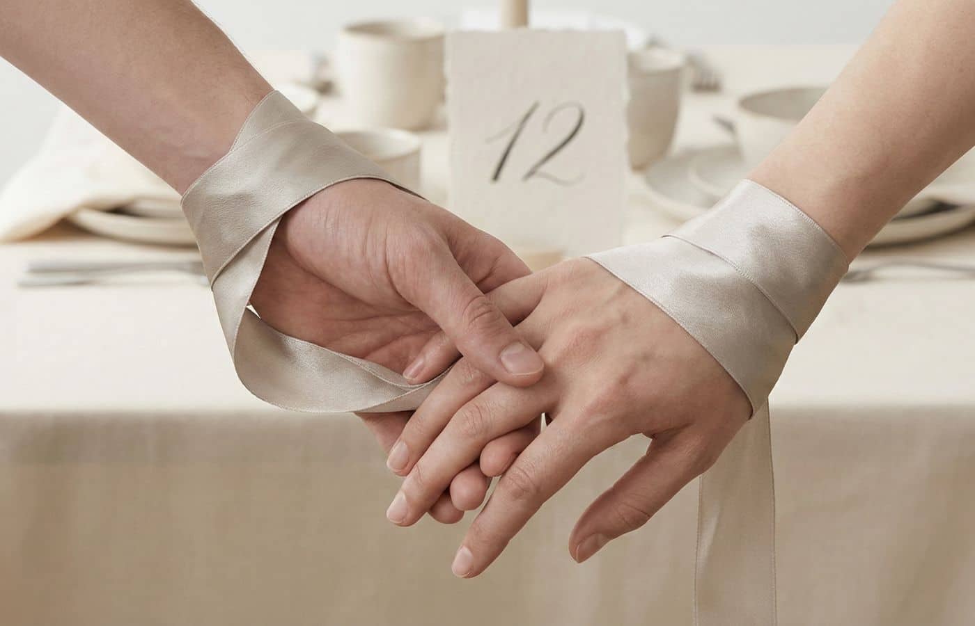 Gros plan esthétique de mains entrelacées par un ruban de soie luxueux pour célébrer les noces de soie (12 ans de mariage)