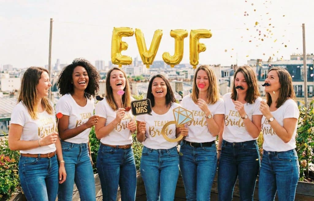 Groupe d'amies riant aux éclats lors d'une activité EVJF originale à Paris : un shooting photo fun avec accessoires de photobooth et confettis.