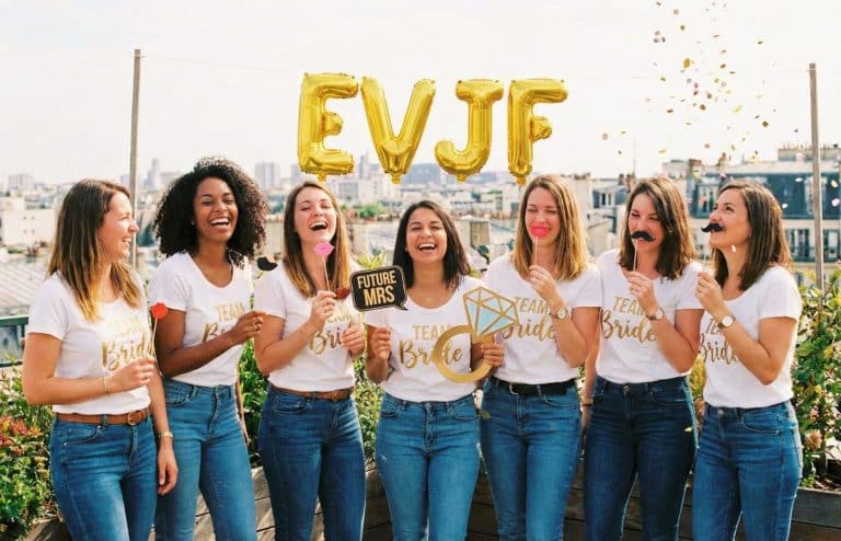 Groupe d'amies riant aux éclats lors d'une activité EVJF originale à Paris : un shooting photo fun avec accessoires de photobooth et confettis.