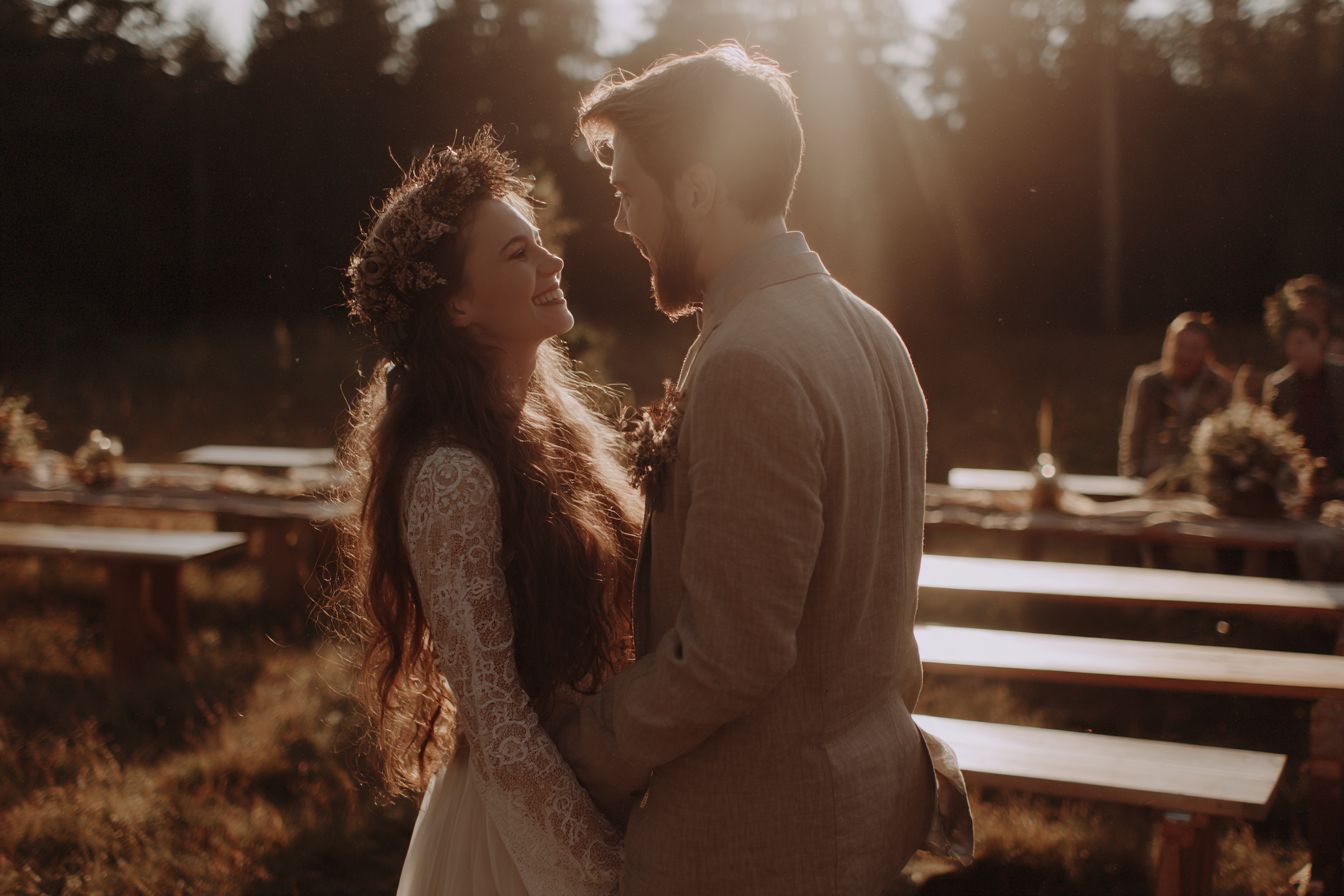 Jeune couple souriant lors d’un mariage éco-responsable dans une clairière au coucher du soleil, décor floral naturel et ambiance chaleureuse.