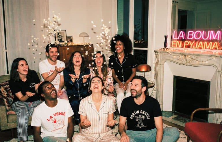 Groupe d'amis adultes riant aux éclats lors d'une soirée pyjama chic à la maison popcorn néon la boom paris france