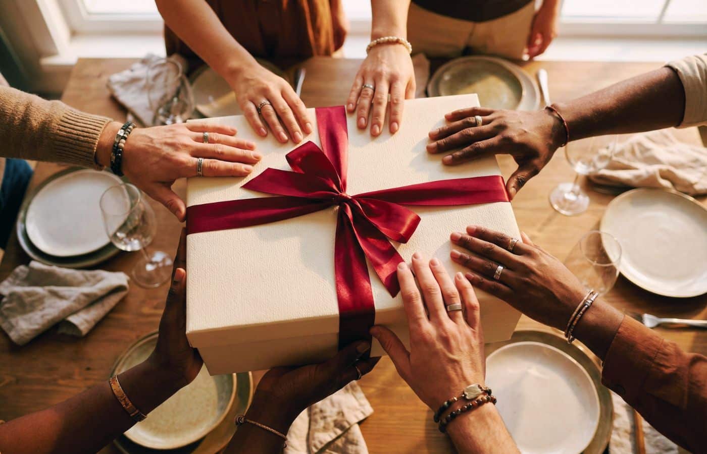 Gros plan sur plusieurs mains d'amis tenant ensemble un cadeau ou un objet symbolique lors d'une fête, illustrant le cadeau commun
