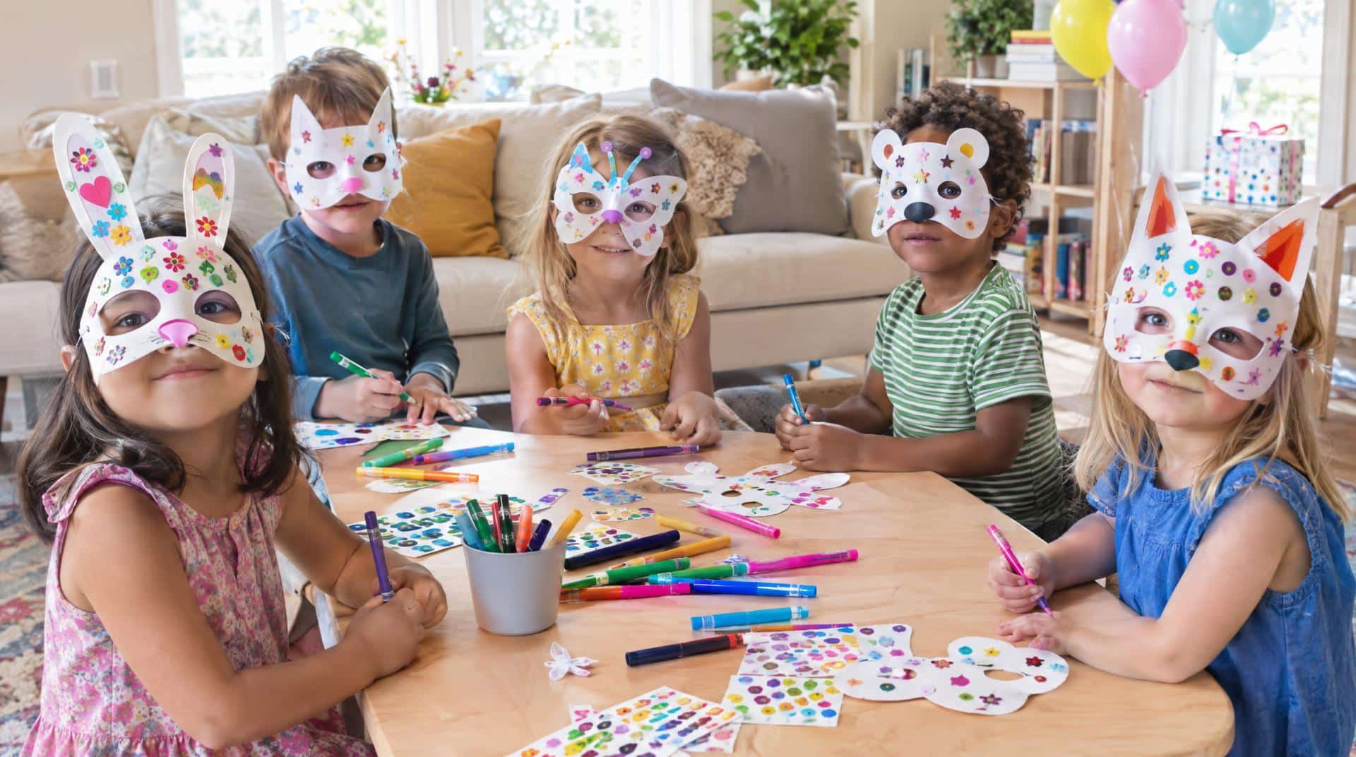 Enfants de 5 ans décorant des masques en carton avec des gommettes, sans peinture
