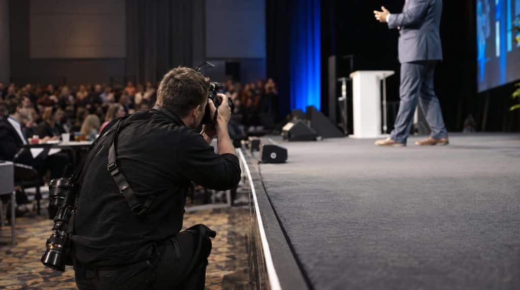 Photographe de reportage accroupi devant la scène d'une conférence d'entreprise