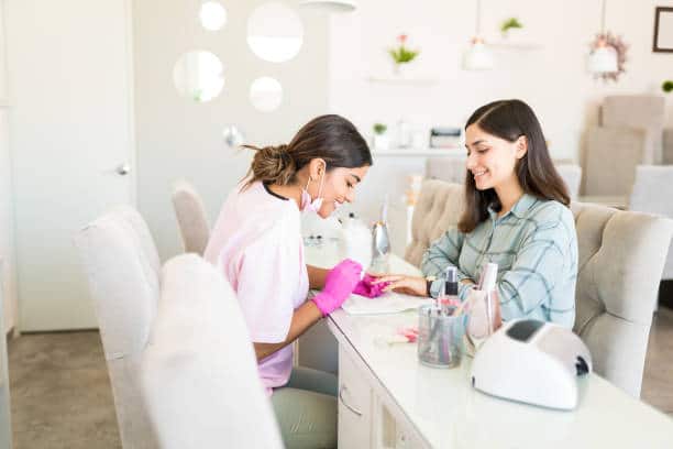 Prothésiste ongulaire qui pose du vernis à une cliente dans un salon d'ongles