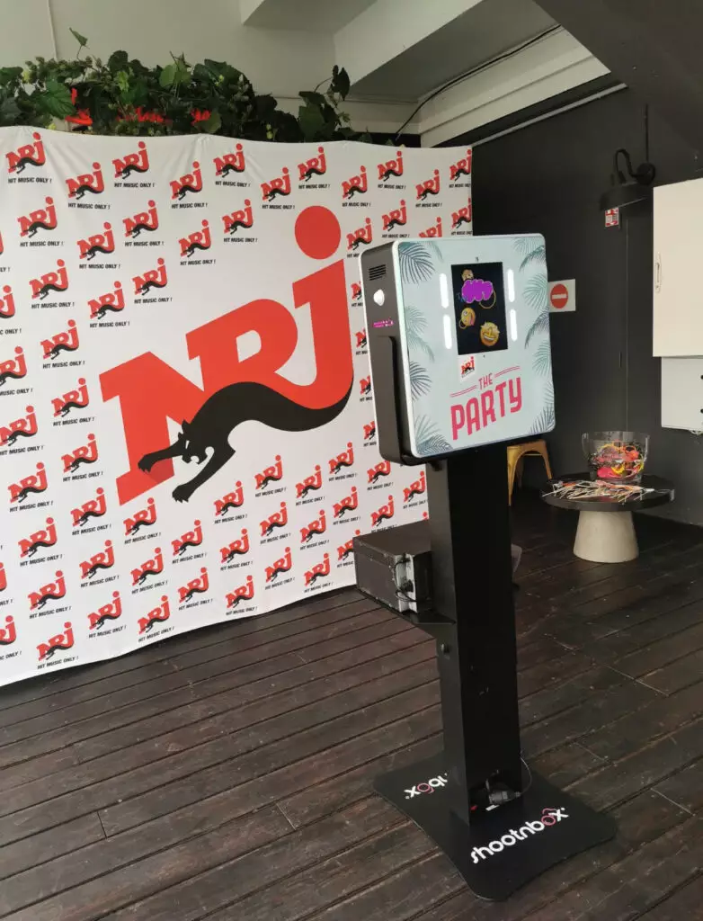 soirée photobooth personnalisé au couleur de la radio NRJ devant un mur avec logo nrj