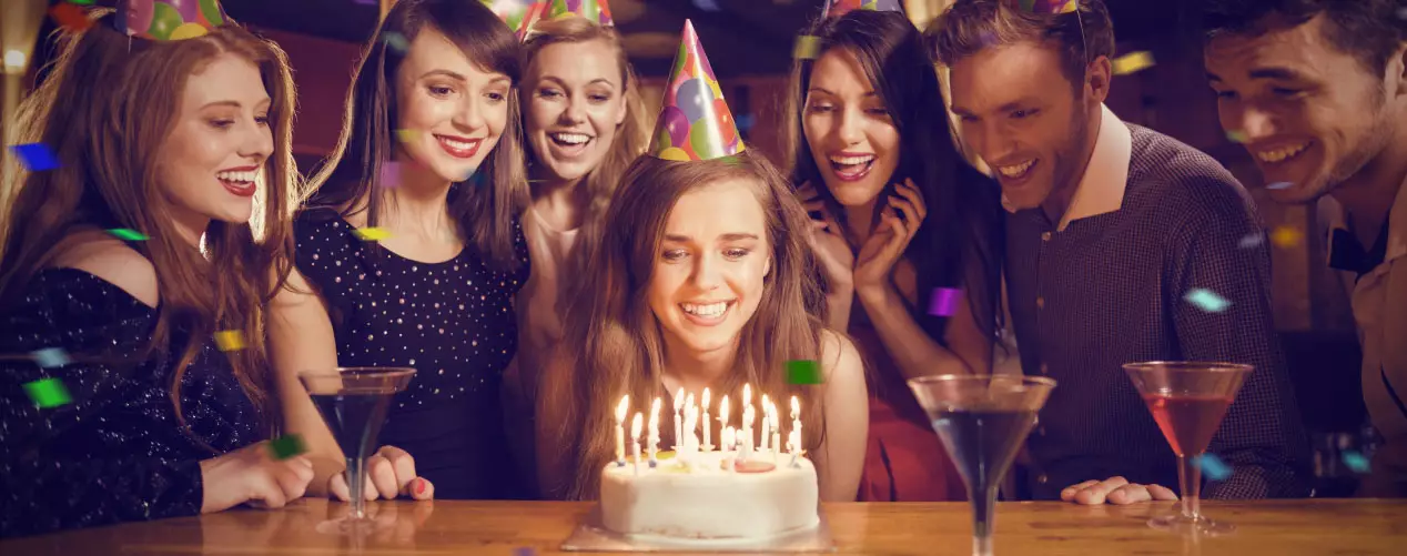 Femme qui souffle sur son gâteau d'anniversaire pour ces 30 ans avec des amis