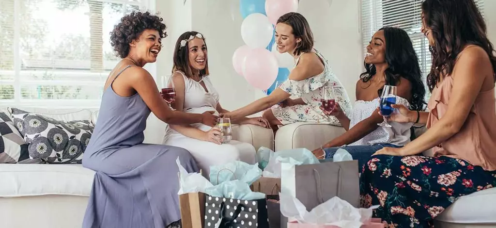 célébration baby shower entre amie future maman avec couronne de fleur dans les cheveux canapé blanc